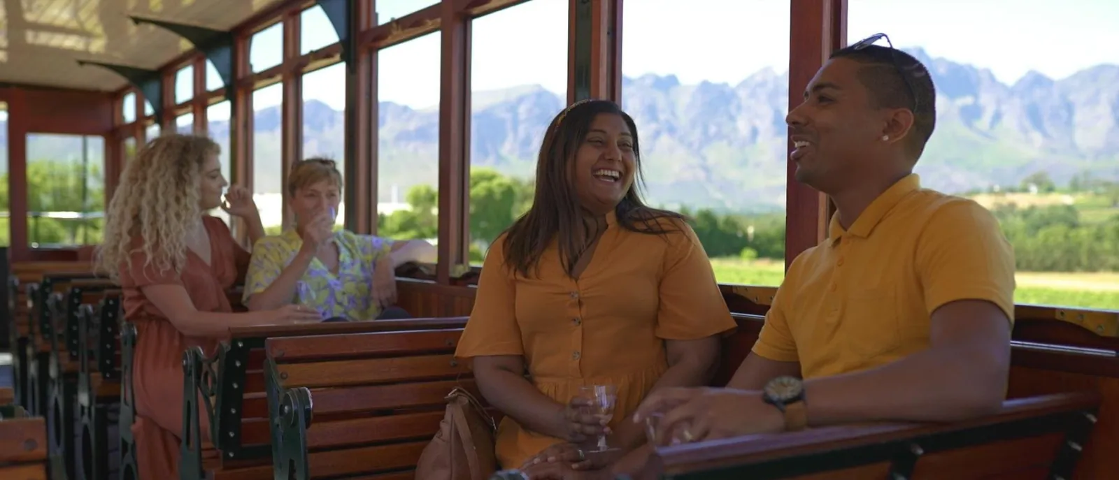 Passengers seated in an open-sided tram carriage with vineyard views