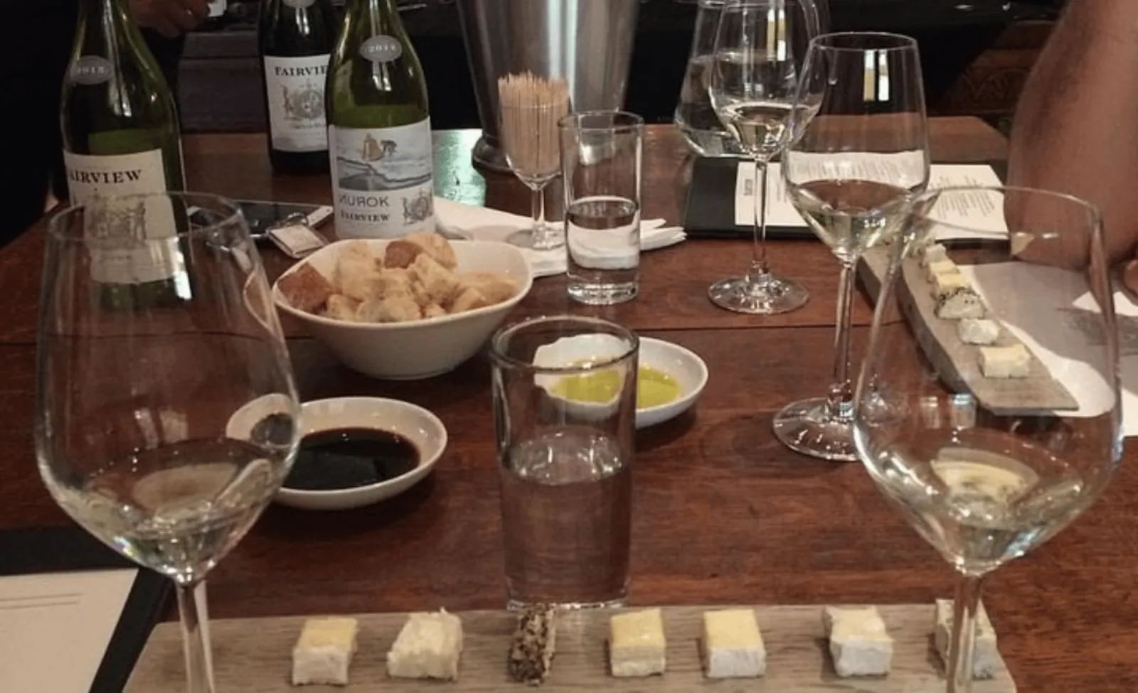 A tasting table set with bottles, glasses and paired cheese and snacks