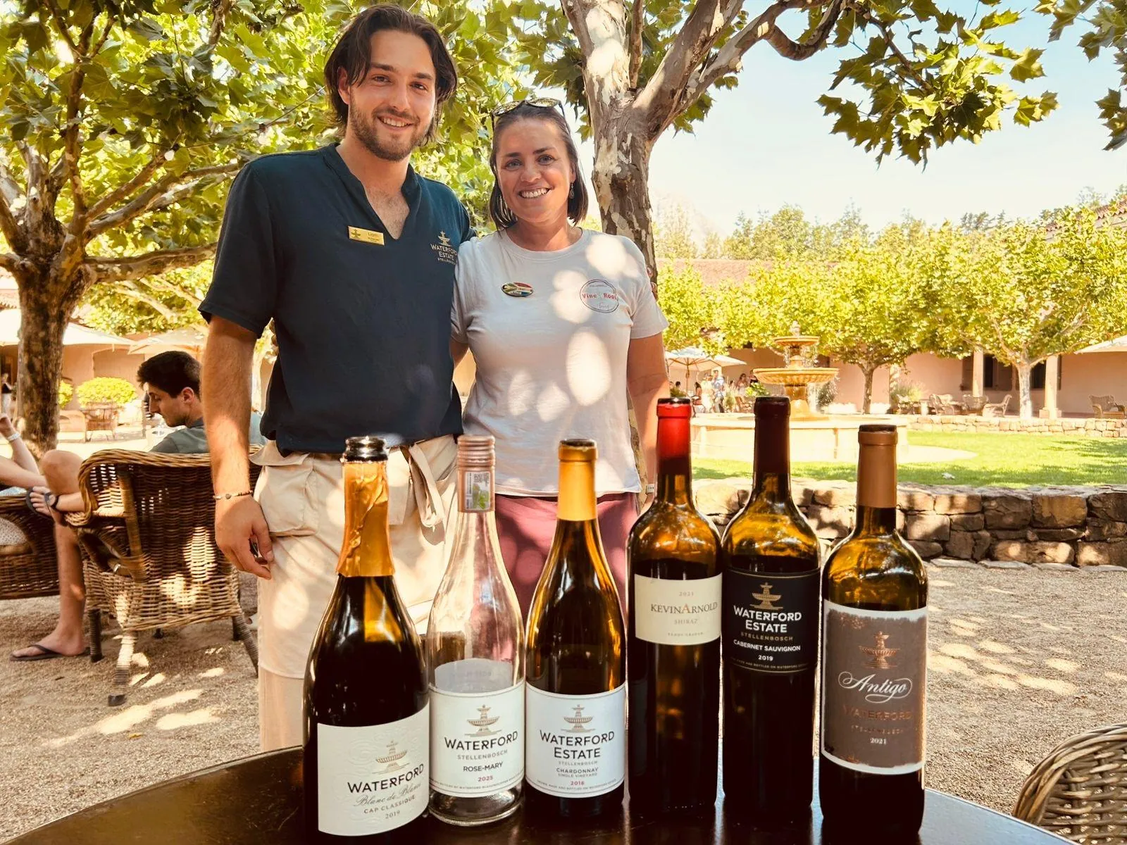 A guide and guest beside a line-up of estate wines at an outdoor tasting